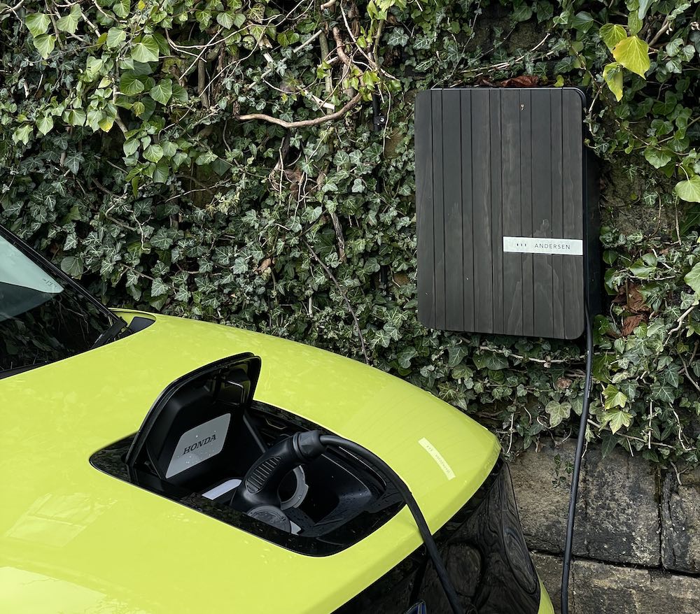 Andersen charging point mounted to a wall covered in ivy, connected to a Honda e